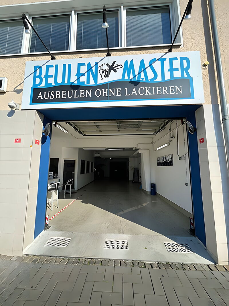 Einfahrt der Beulenmaster-Werkstatt mit Schild „Ausbeulen ohne Lackieren“
